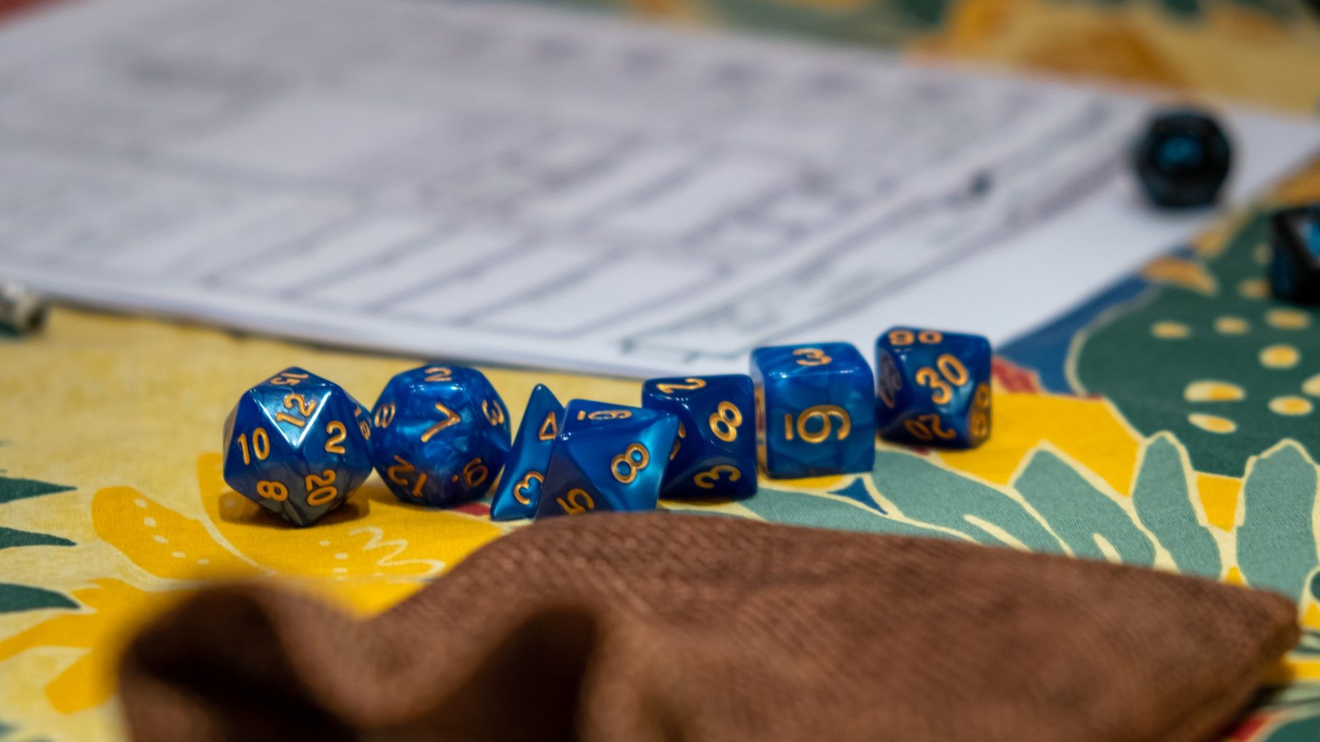 A set of seven blue polyhedral dice on a table in front of a character s