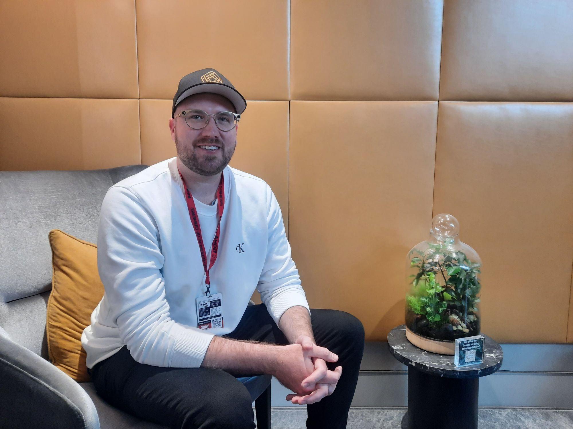 Stephen Cornish, a white man in a long-sleeve white shirt, black jeans, and black cap, smiles at the camera. 