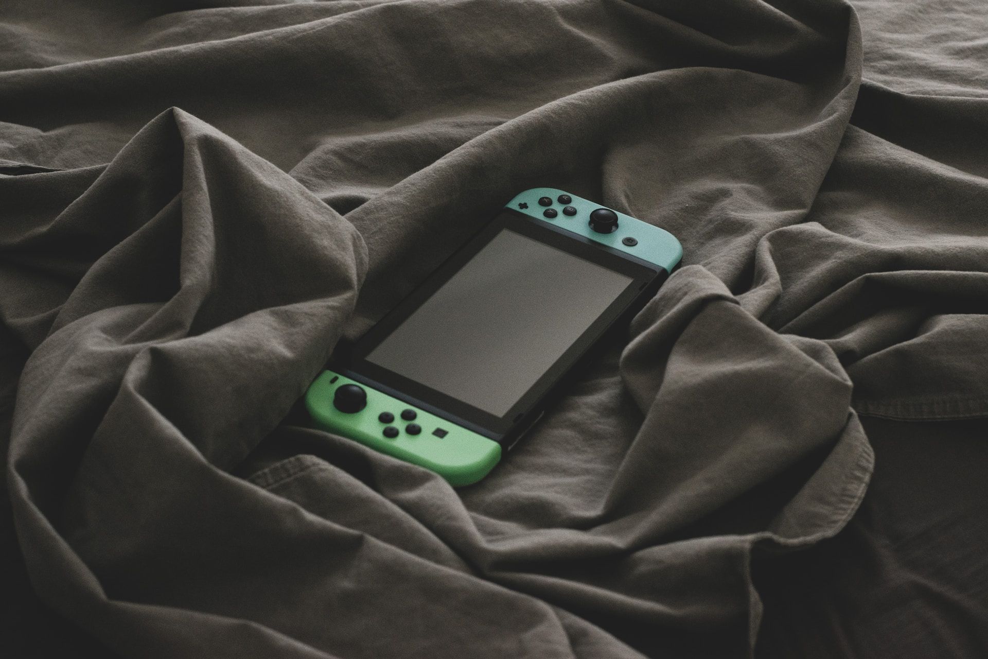 A Nintendo Switch with blue and green JoyCons sitting on a wrinkled grey bedsheet.